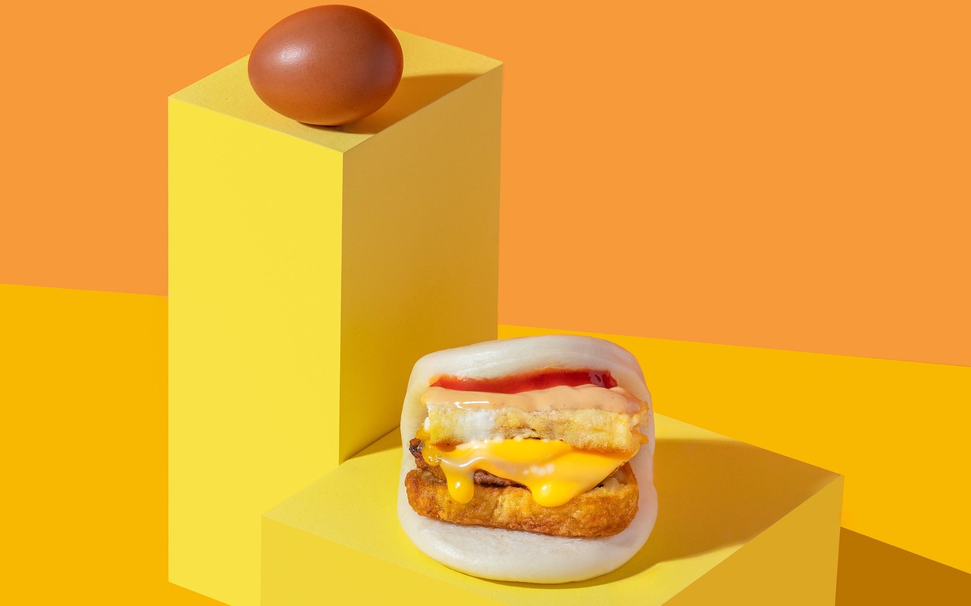 Breakfast Bao with cheese, egg, and sauce on a yellow platform with an orange background